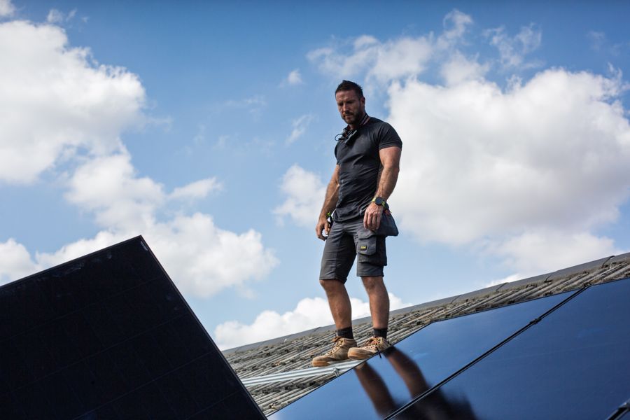 A PowerHaus installer standing on the finished row of all-black solar panels in Llantrisant